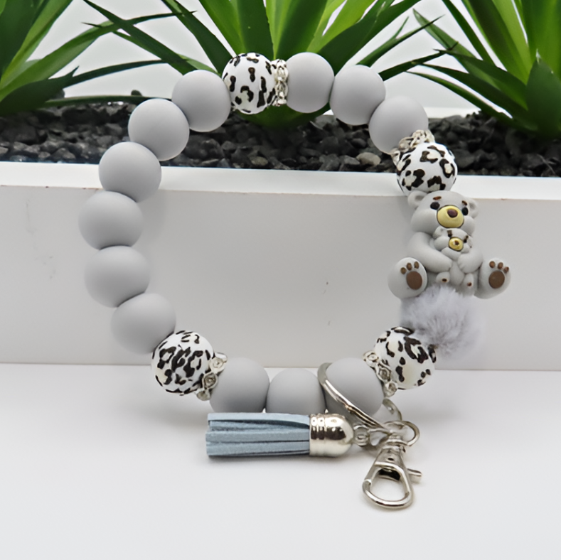 Bracelet with gray beads, animal print charms, and a tassel on a white surface with green plants in the background.
