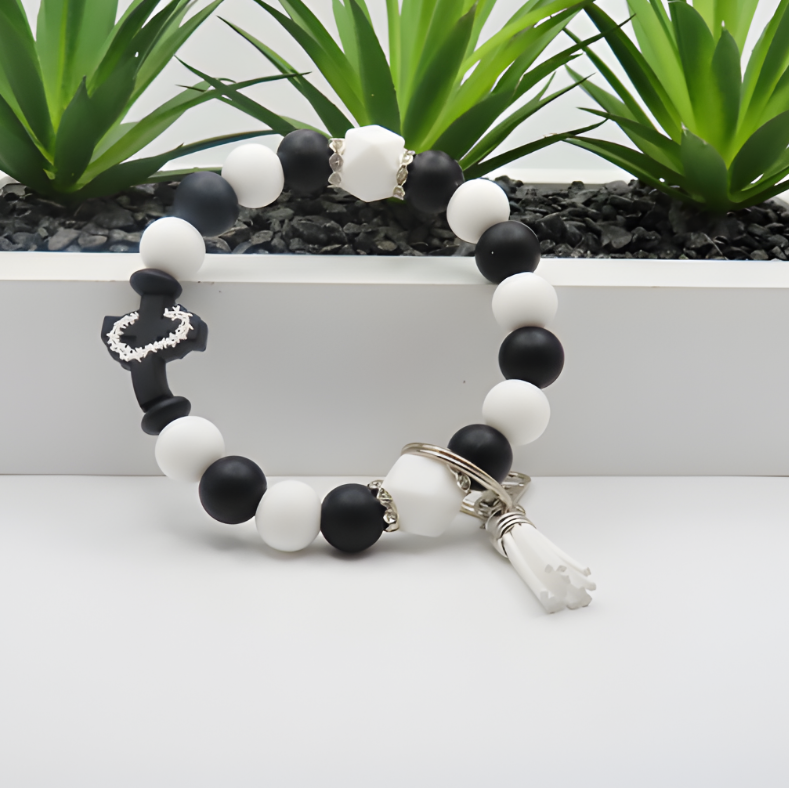 Black and white beaded bracelet with keychain on a white surface with plants in the background