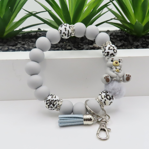 Bracelet with gray beads, leopard print charms, and a tassel keychain on a white surface with plants in the background.
