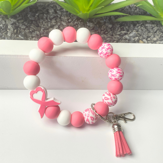 Pink and white beaded bracelet with a breast cancer awareness charm on a white surface.