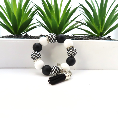 Black, white, and checkered bracelet on a white surface with green plants in the background
