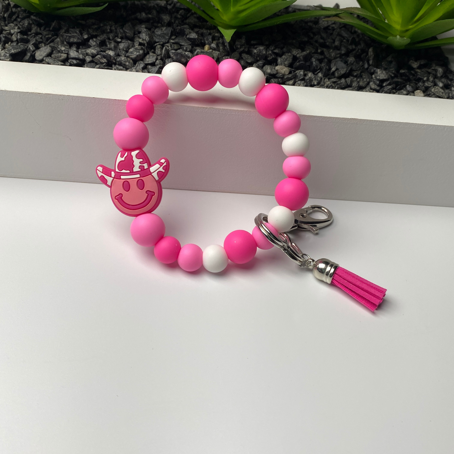 Pink and white beaded keychain with a smiley face charm on a white surface.