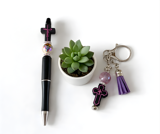 Black pen with decorative elements, small potted succulent, and keychain with cross and tassel on a white background