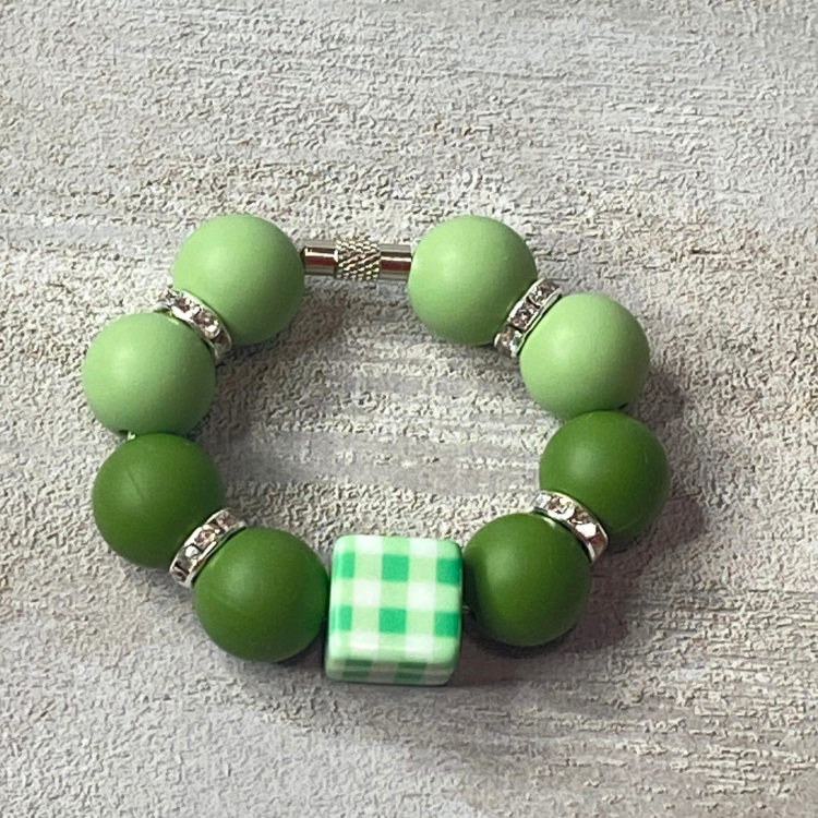 Green beaded bracelet with a checkered cube charm on a textured gray surface