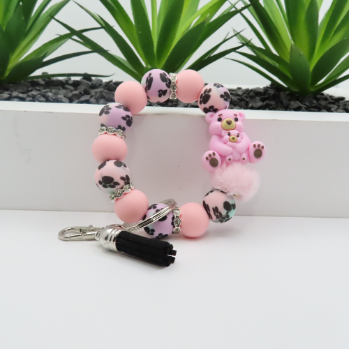 Pink beaded keychain with a small bear charm on a white surface with plants in the background