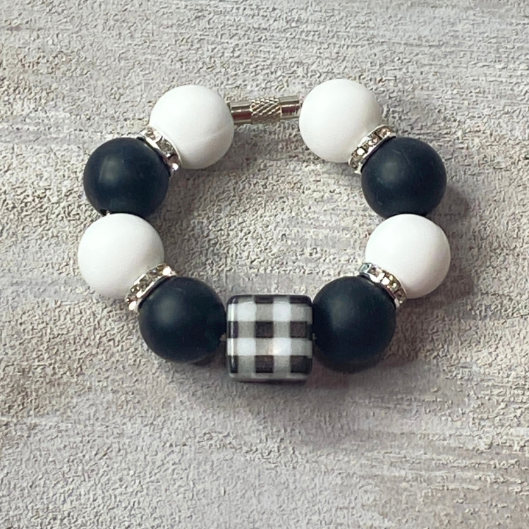 Bracelet with black, white, and plaid beads on a textured surface