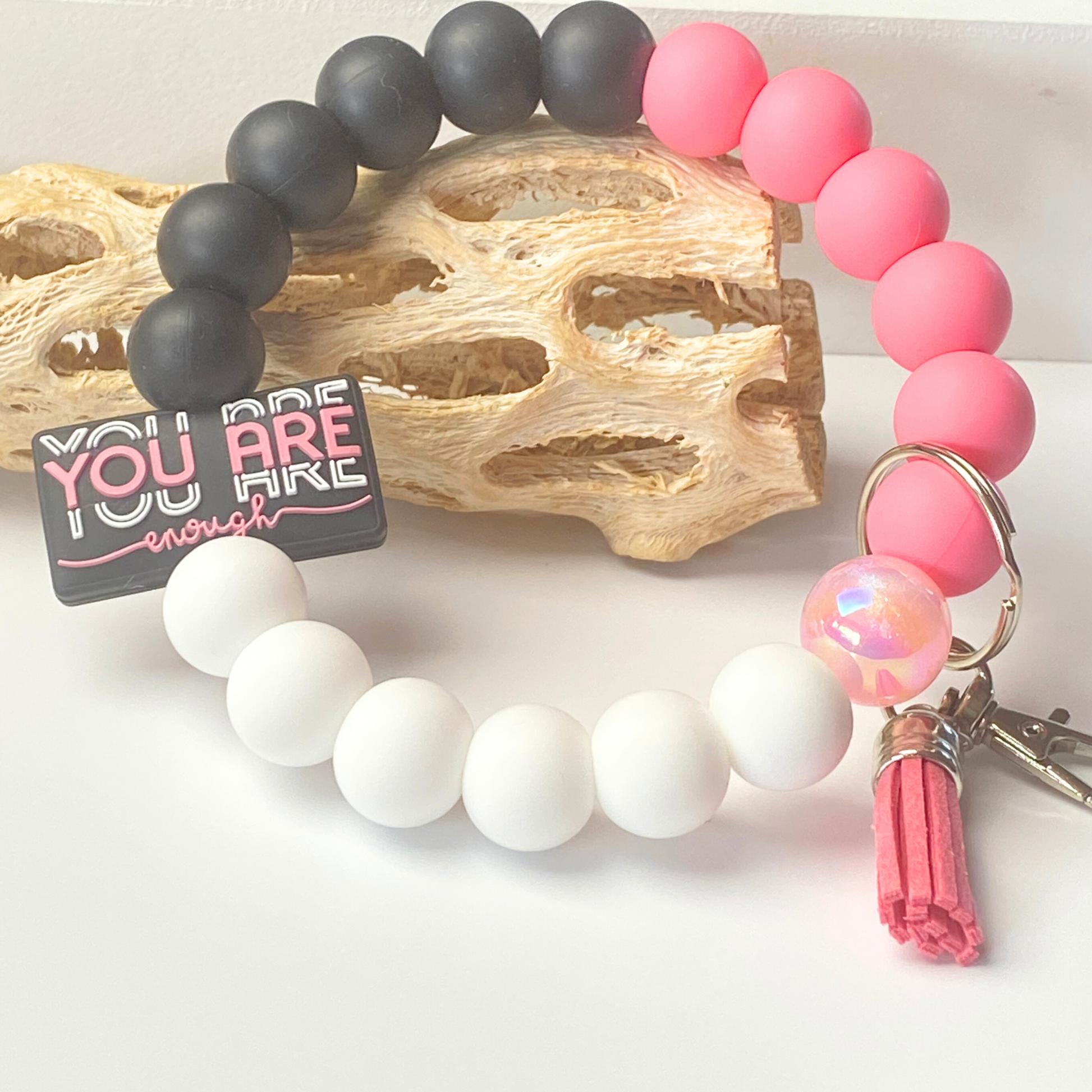 Beaded bracelets with pink, black, and white beads, and a keychain with a motivational tag.