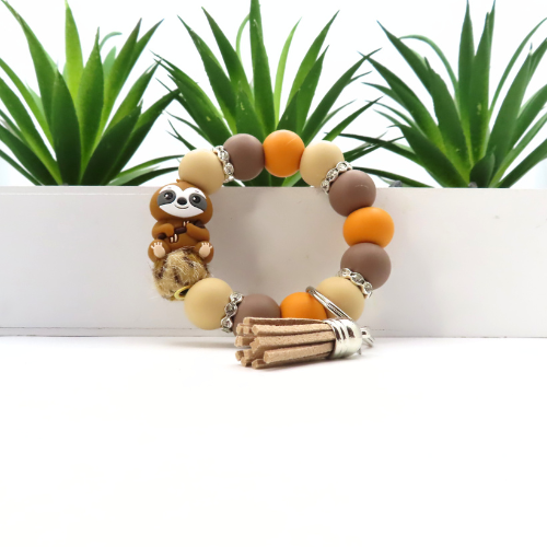 Bracelet with sloth charm and wooden sticks on a white surface with plants in the background