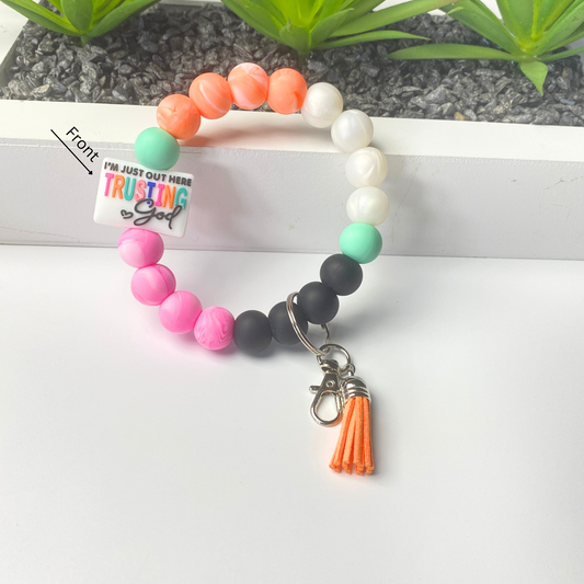 Colorful beaded bracelet with a tassel charm on a white surface, with a plant in the background.