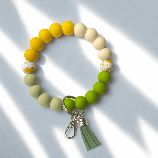 Beaded bracelet with yellow, green, and beige beads and a green tassel charm on a light background.