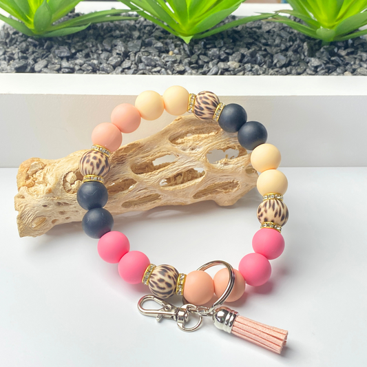 Colorful beaded bracelet with a keychain on a white surface with a natural wood piece and green plants in the background.