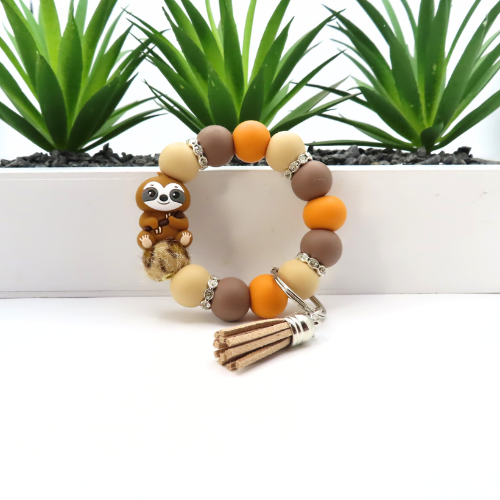 Beaded bracelet with sloth charm and tassel on a white surface with plants in the background