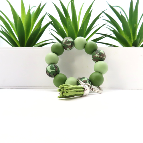 Green beaded bracelet with tassel on a white surface with plants in the background