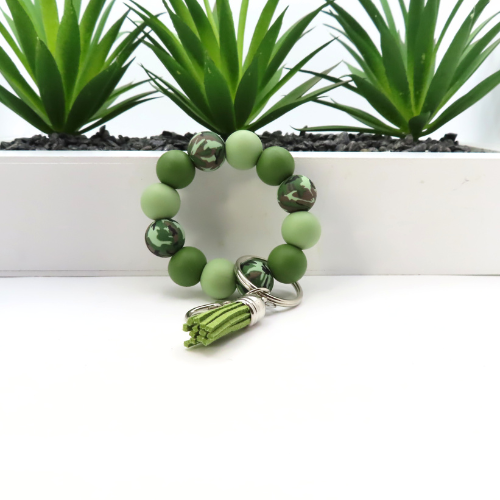 Green beaded bracelet with a keychain on a white surface with plants in the background