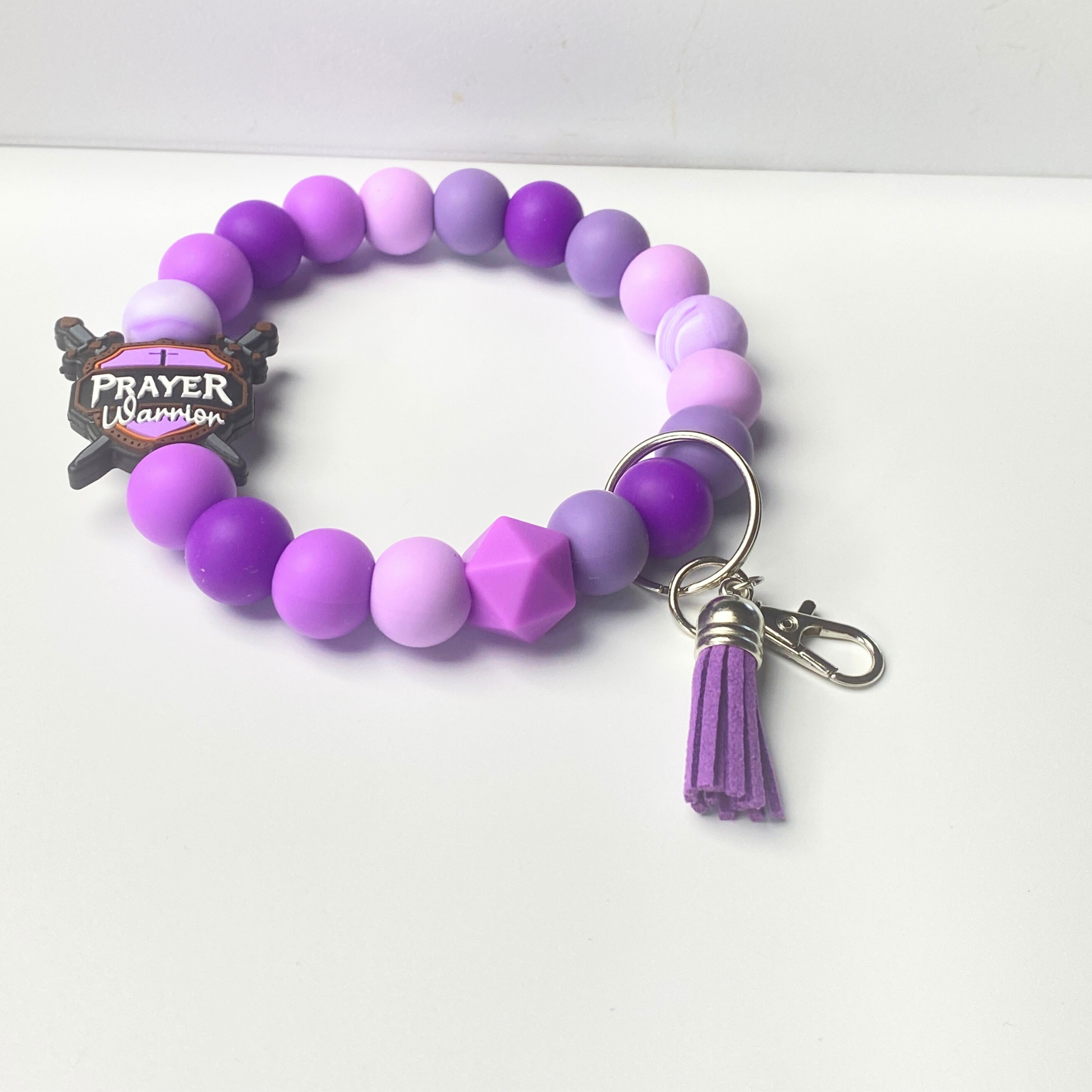 Purple beaded bracelet with a tassel charm on a white background