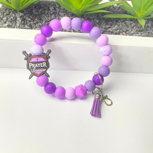 Purple beaded bracelet with a 'Prayer Warrior' charm on a white background