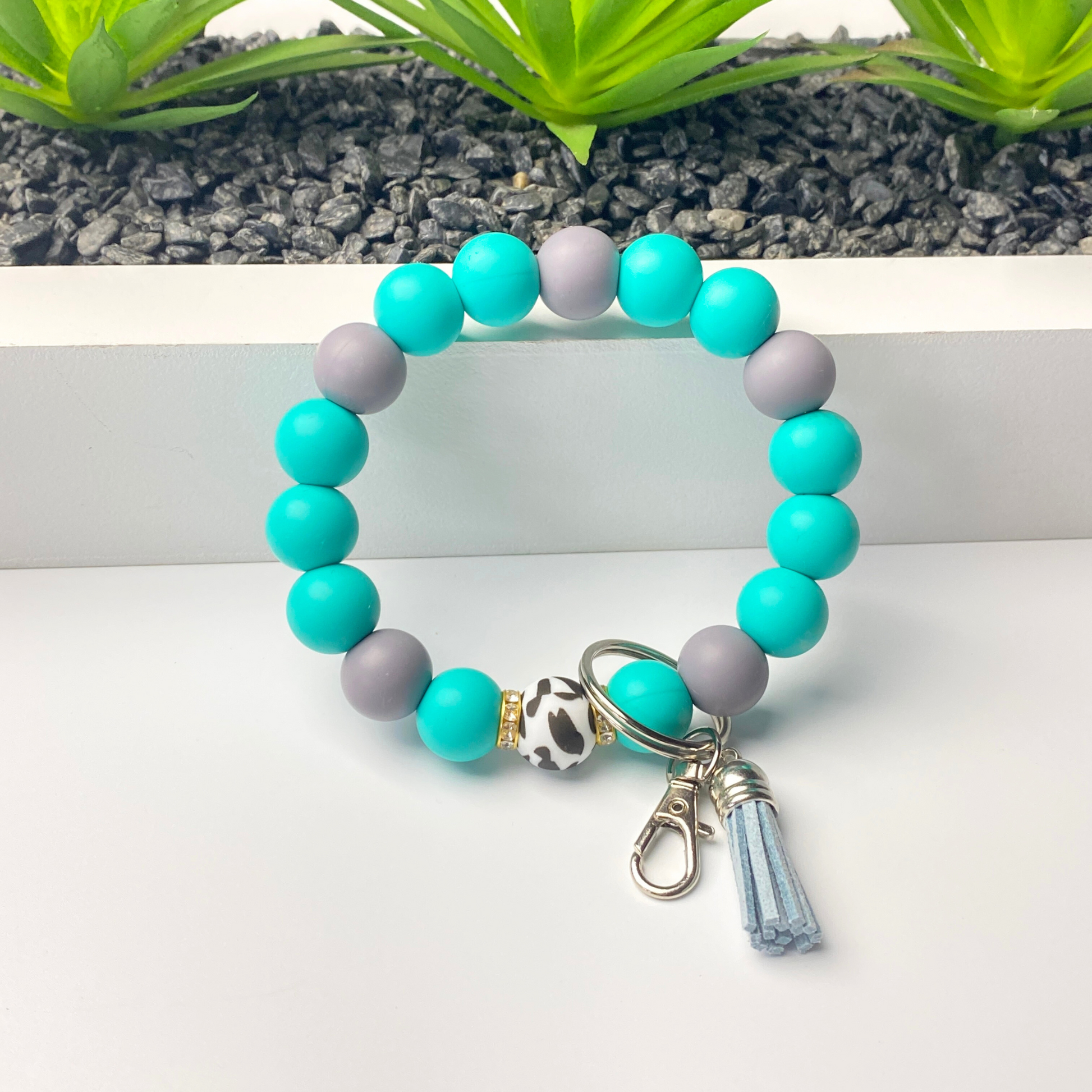 Beaded bracelet with turquoise and gray beads and a keychain charm on a white surface.