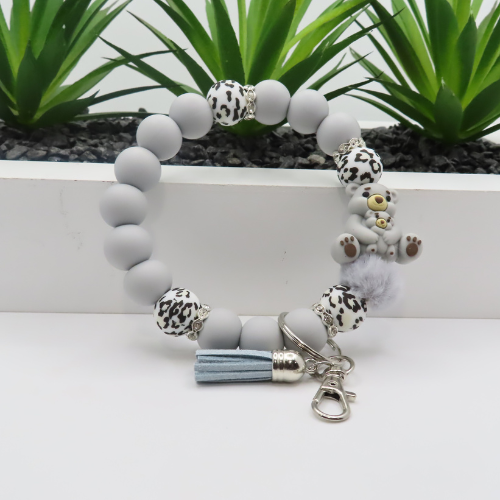 Gray beaded bracelet with dalmatian print charms and a tassel on a white surface with green plants in the background.