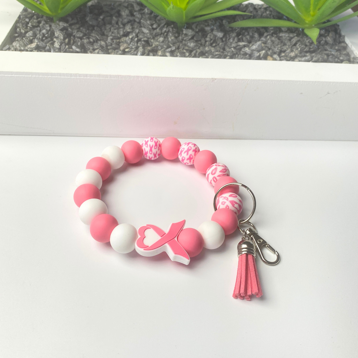 Pink and white beaded keychain with a breast cancer awareness ribbon charm on a white surface.