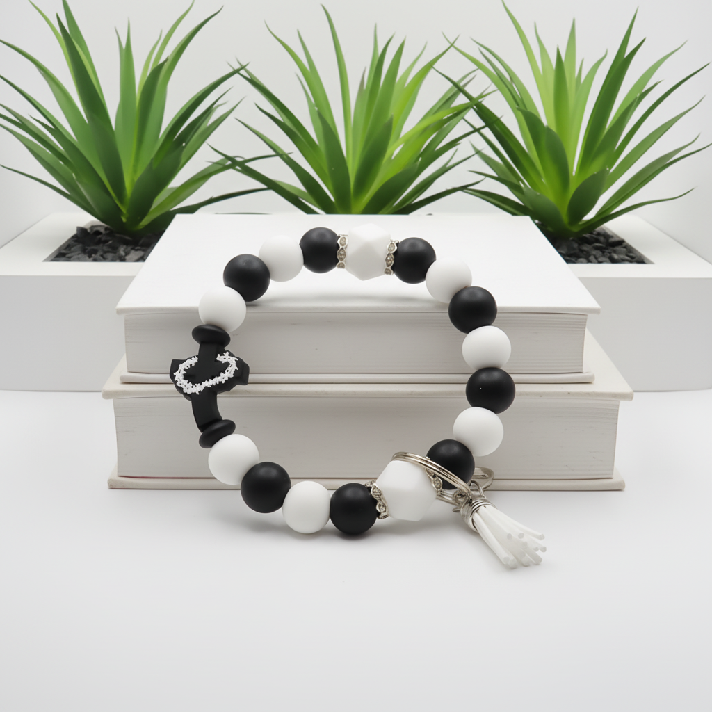 Black and white beaded bracelet with a keychain on a white surface with green plants in the background