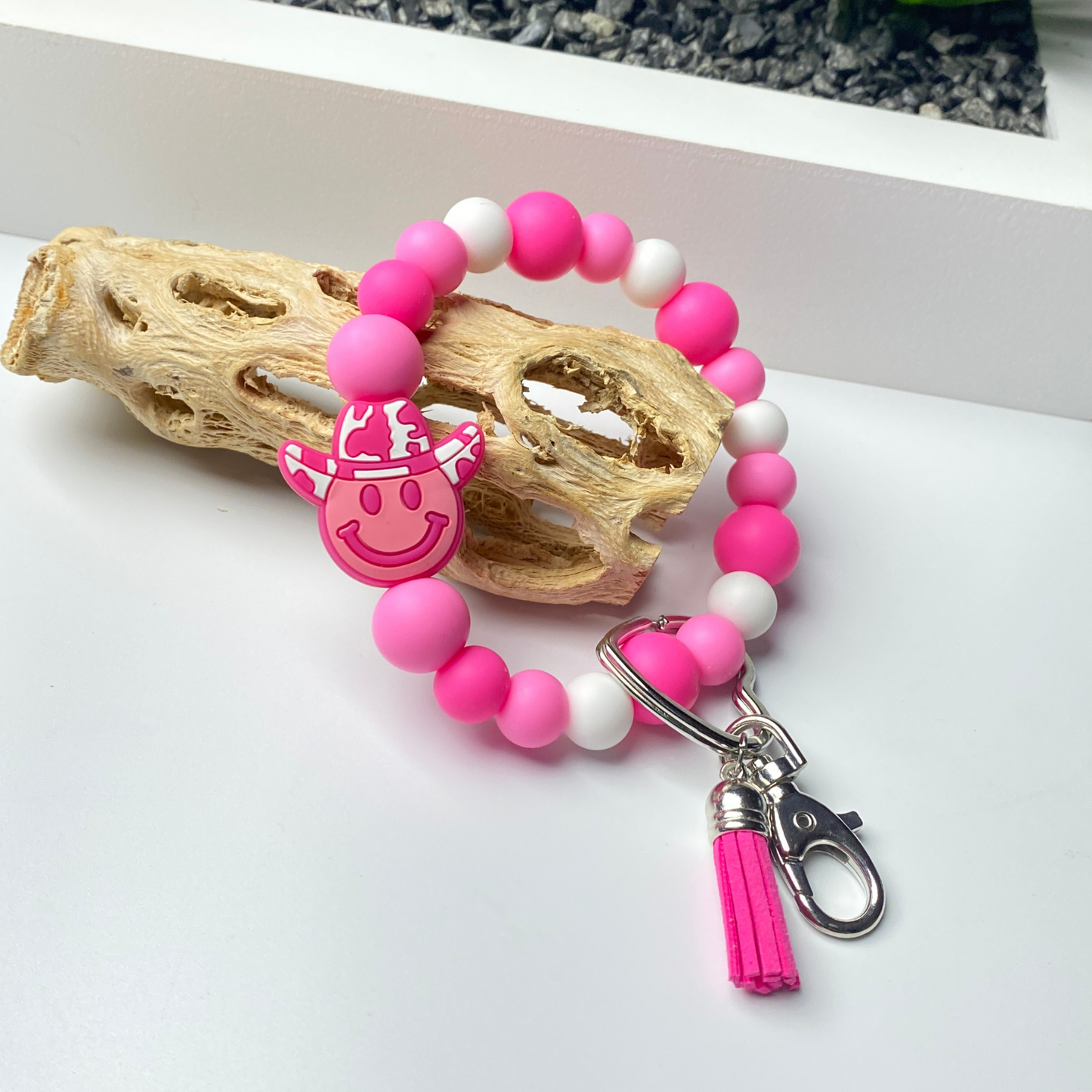 Pink and white beaded keychain with a smiley face charm on a white surface.