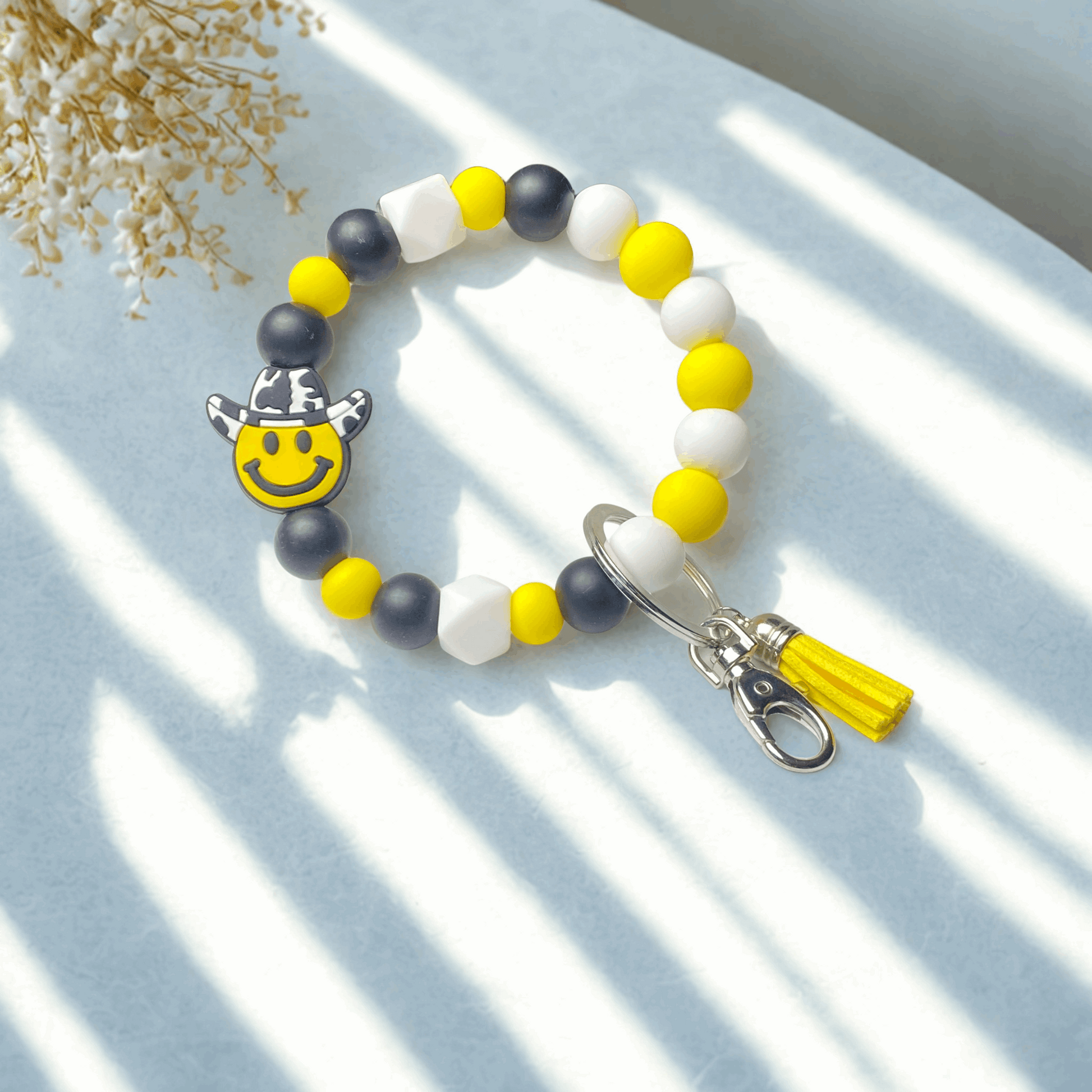 Colorful beaded keychain with a smiley face charm on a light blue surface.