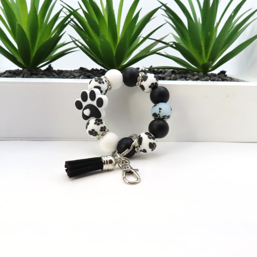 Black and white beaded bracelet with paw print charm on a white surface with plants in the background