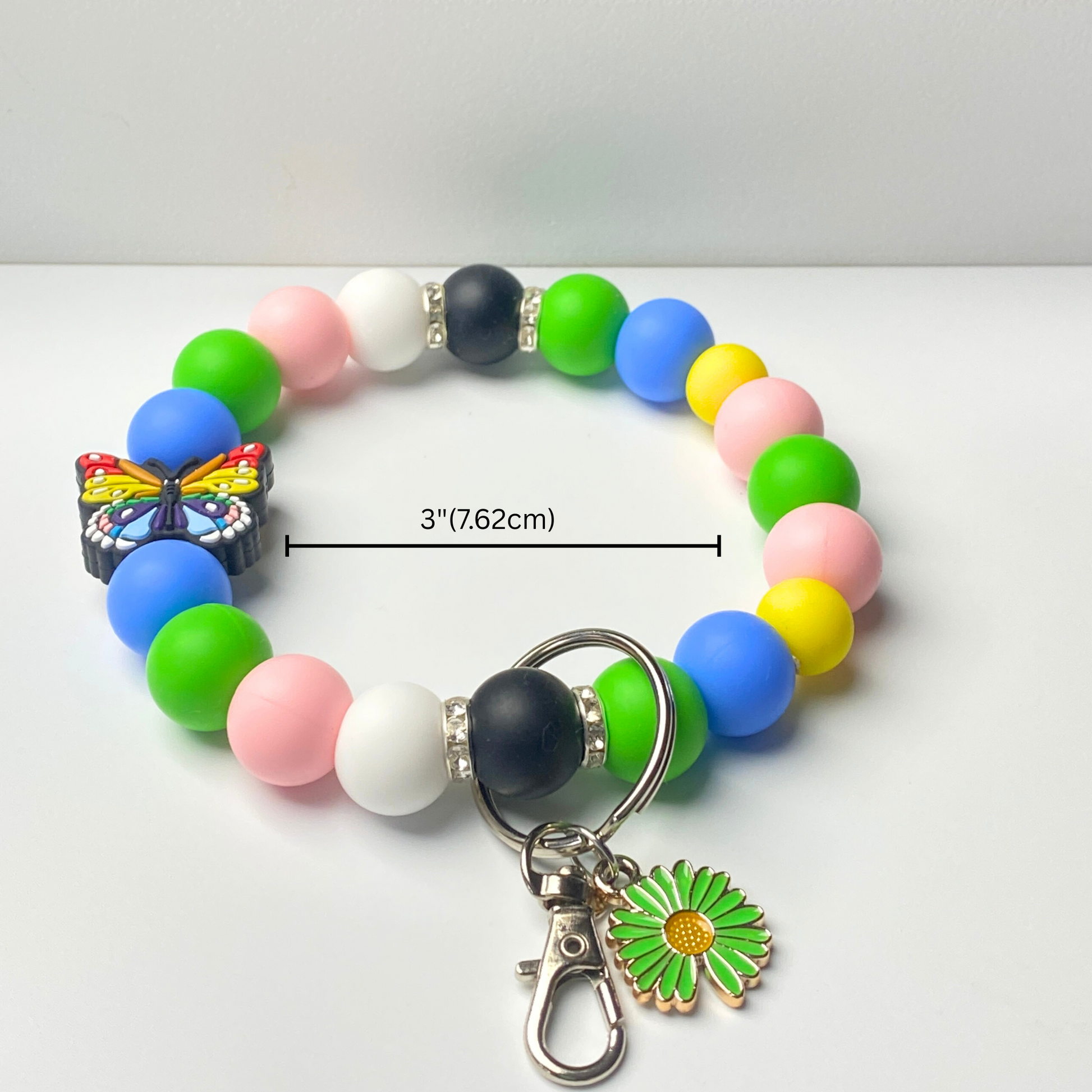 Colorful beaded bracelet with a butterfly charm and flower keychain on a white background