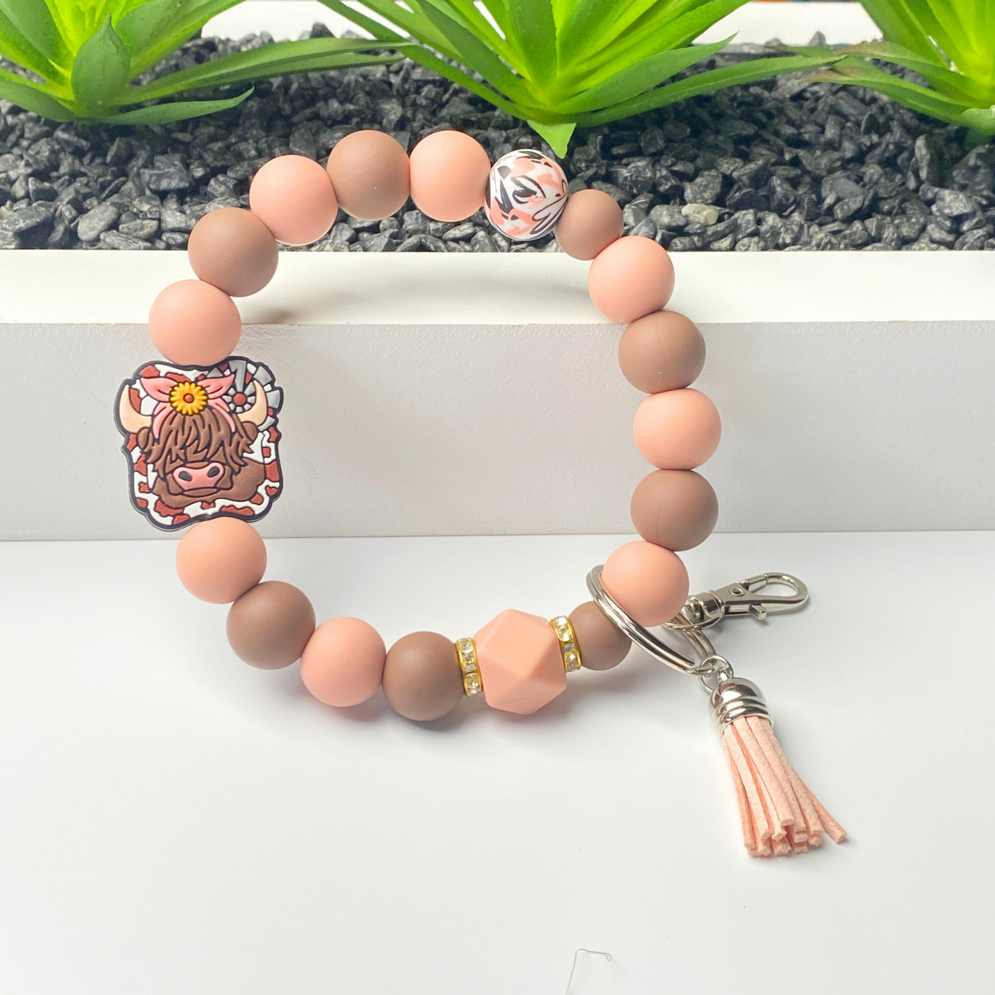 Beaded bracelet with a keychain attachment on a white surface with greenery in the background