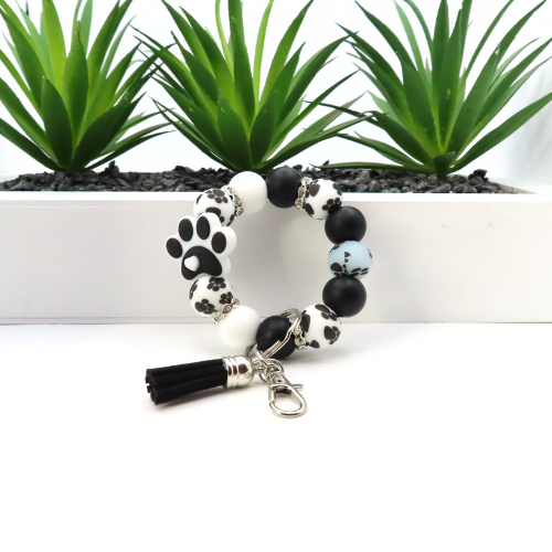 Bracelet with paw print charm and tassel on a white background with plants in the background