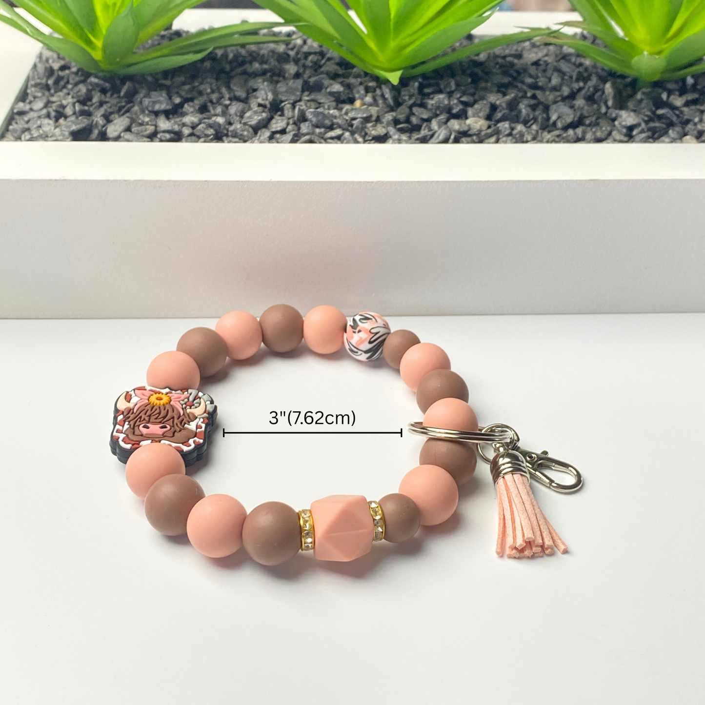 Beaded bracelet with a keychain on a white surface, featuring measurements.