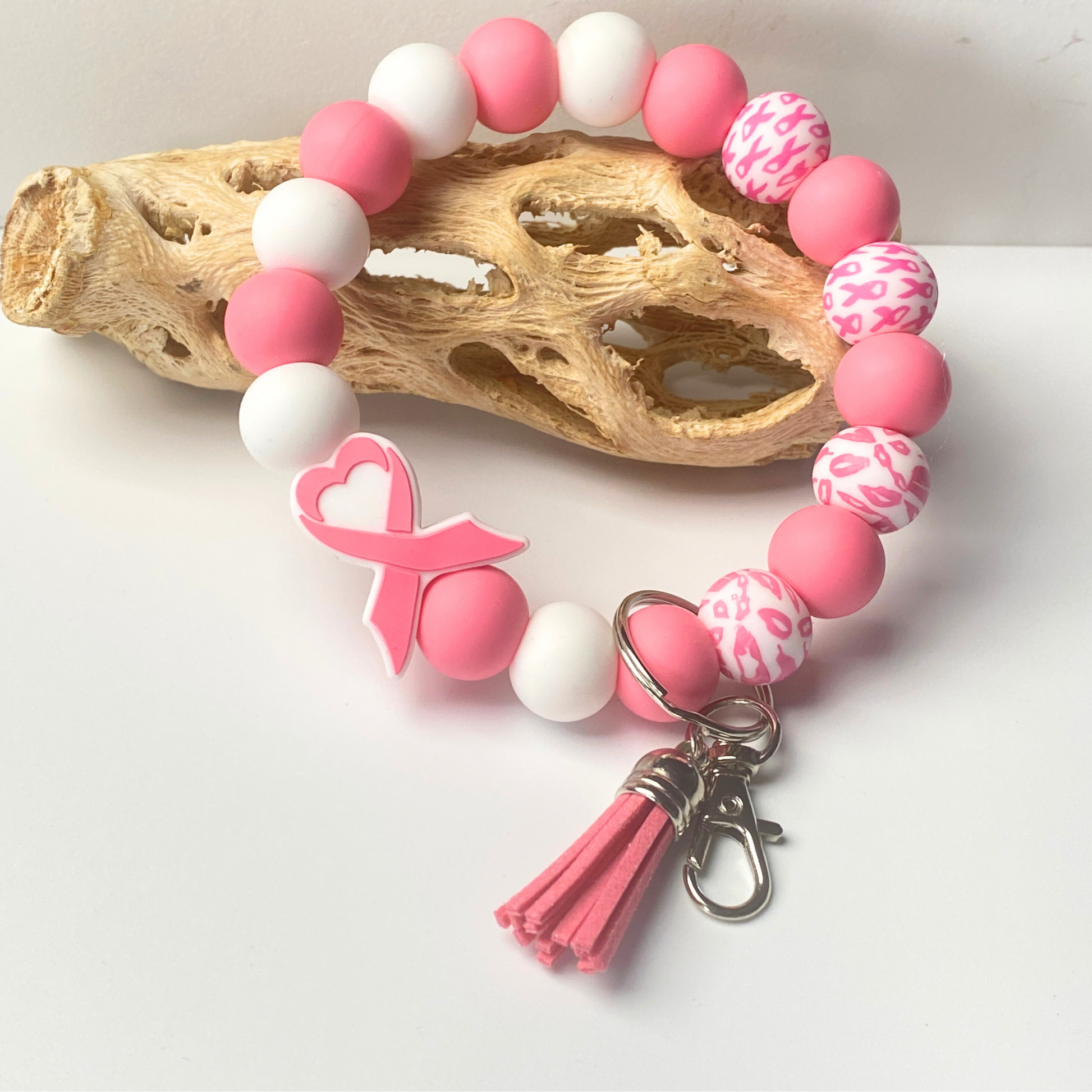 Pink and white beaded bracelet with a breast cancer awareness ribbon charm on a light background.