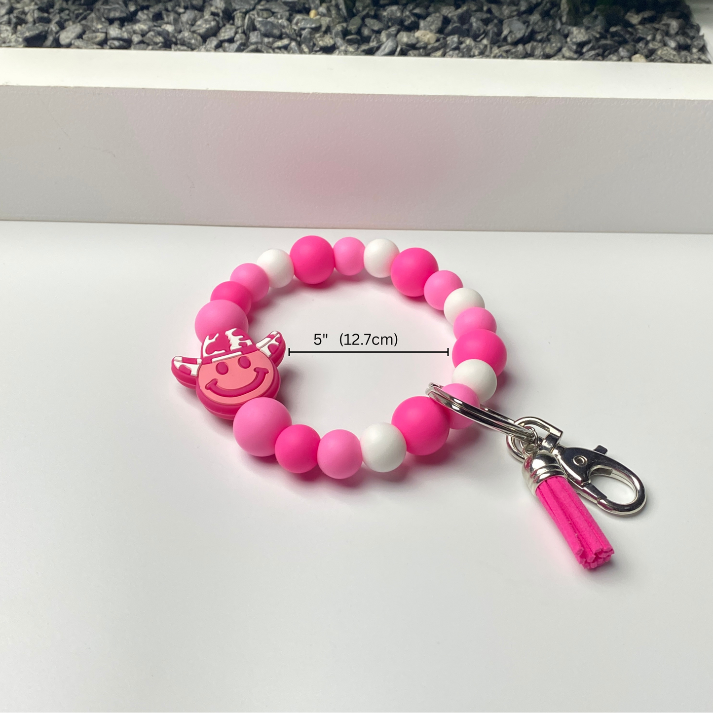 Pink and white beaded keychain with a smiley face charm on a white surface.