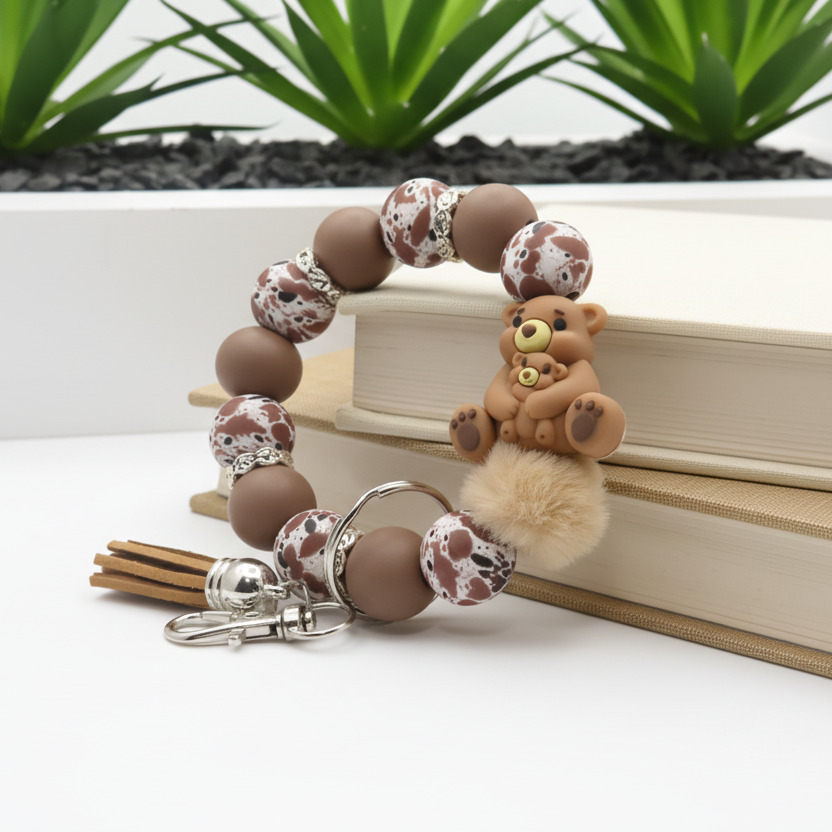 Bracelet with teddy bear charm and keychain on a white surface with plants in the background