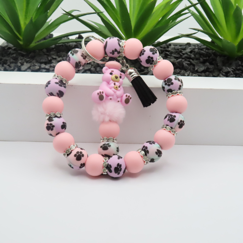 Pink beaded bracelet with paw print design on a white surface with green plants in the background