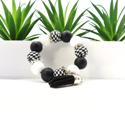 Bracelet with black, white, and checkered beads on a white surface with green plants in the background