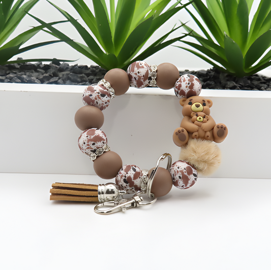 Bracelet with teddy bear charm and keychain on a white surface with plants in the background