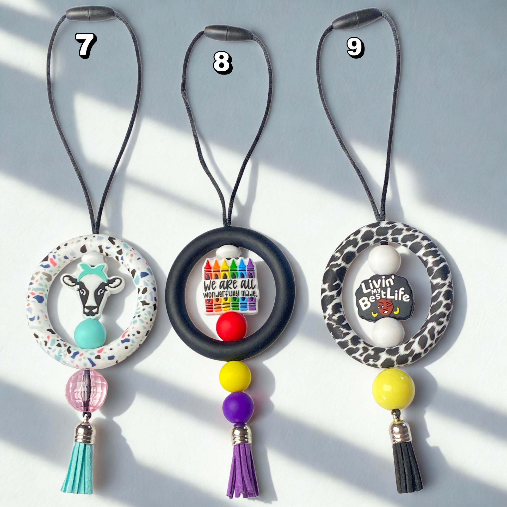 Three decorative keychains with beads and tassels on a light gray background