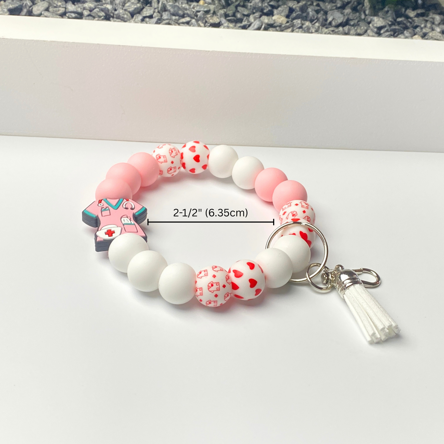 Bracelet with pink and white beads and a cross charm on a white surface.