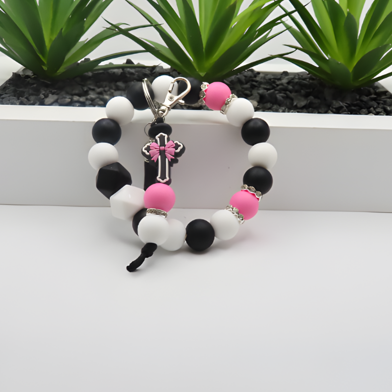 Bracelet with black, white, and pink beads on a white surface with plants in the background