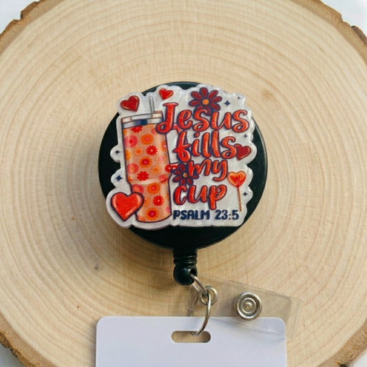 Retractable badge holder with 'Jesus fills my cup' design on a wooden background