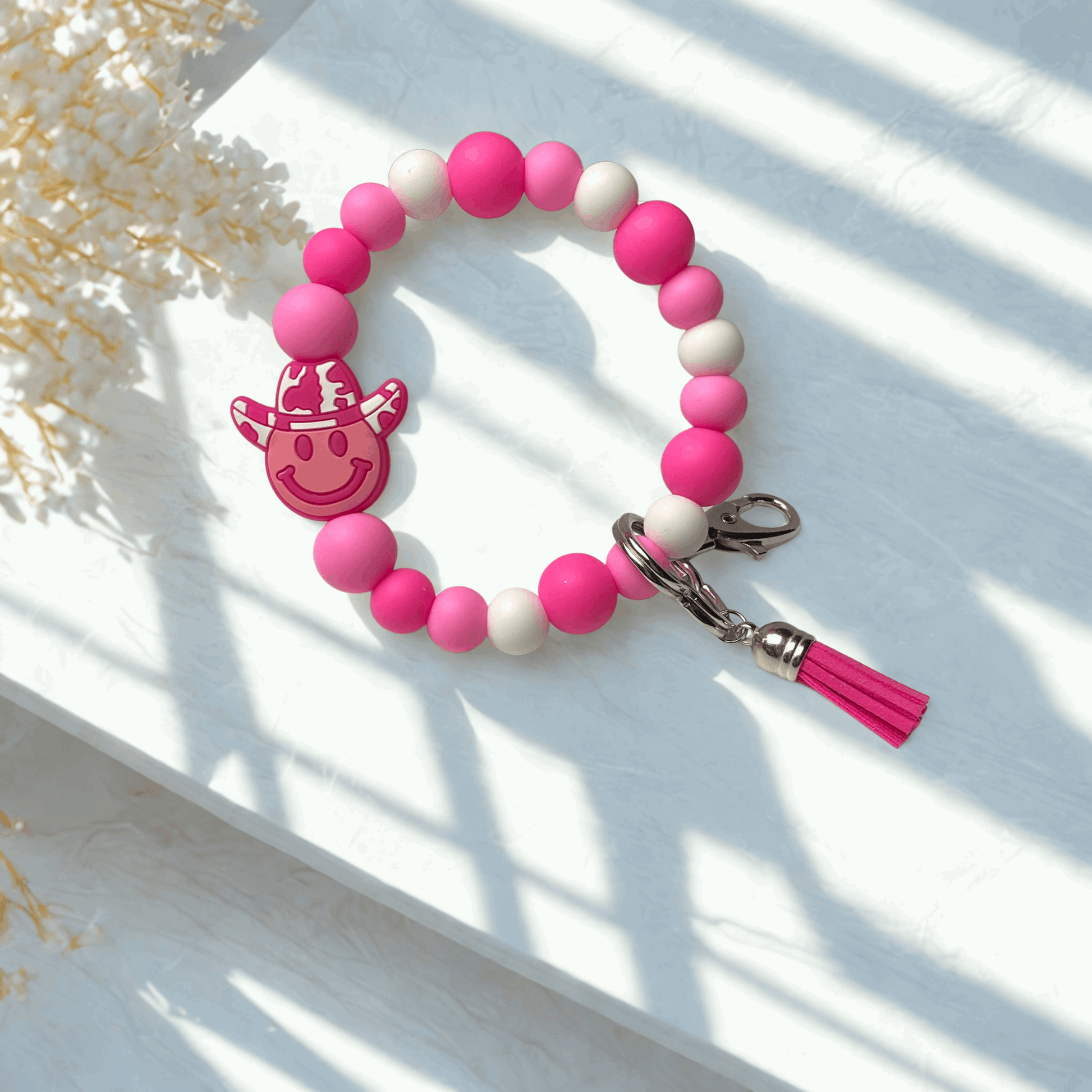 Pink and white beaded keychain with a smiley face charm on a light wooden surface.