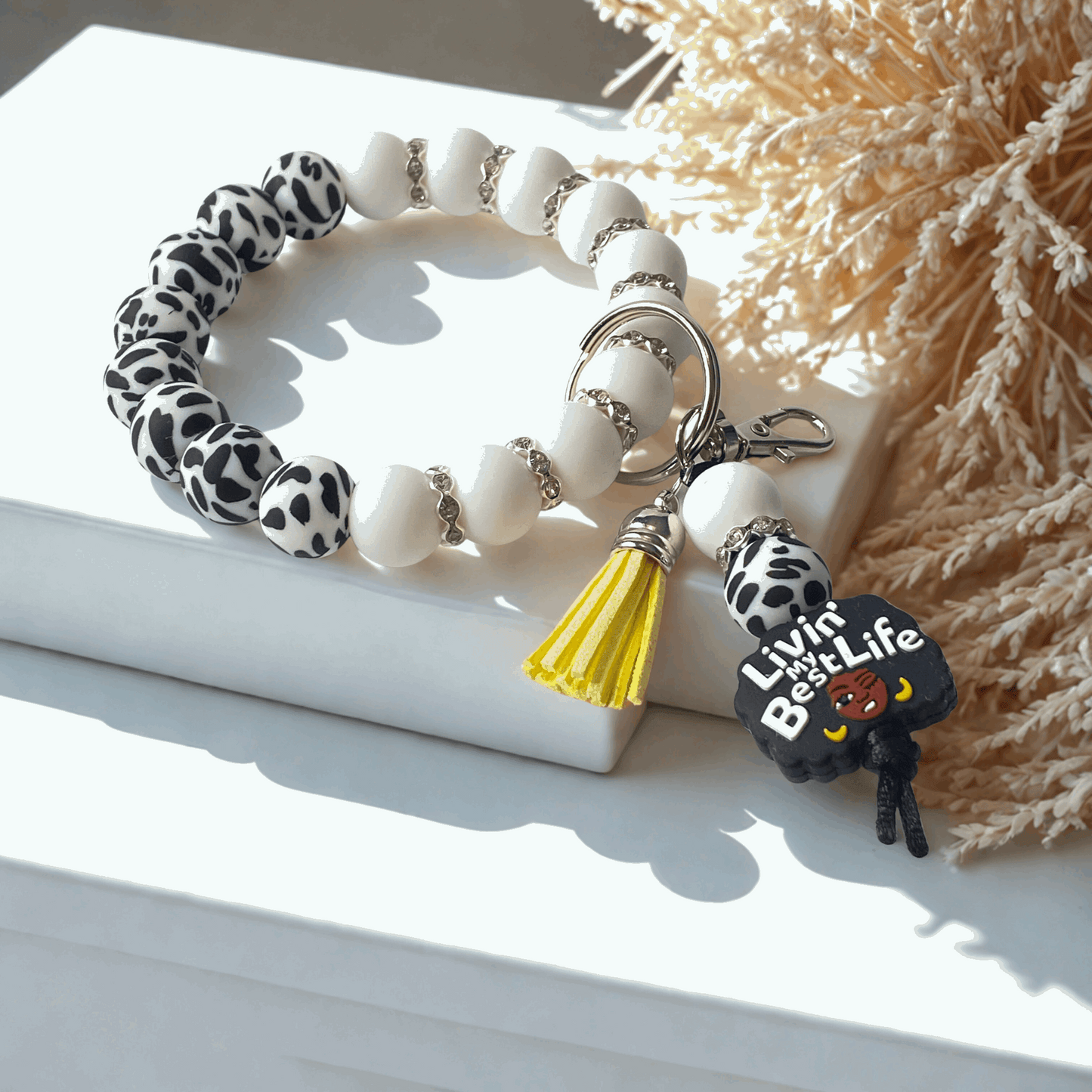 Bracelet with white beads, leopard print accents, and a keychain with a yellow tassel on a light surface.