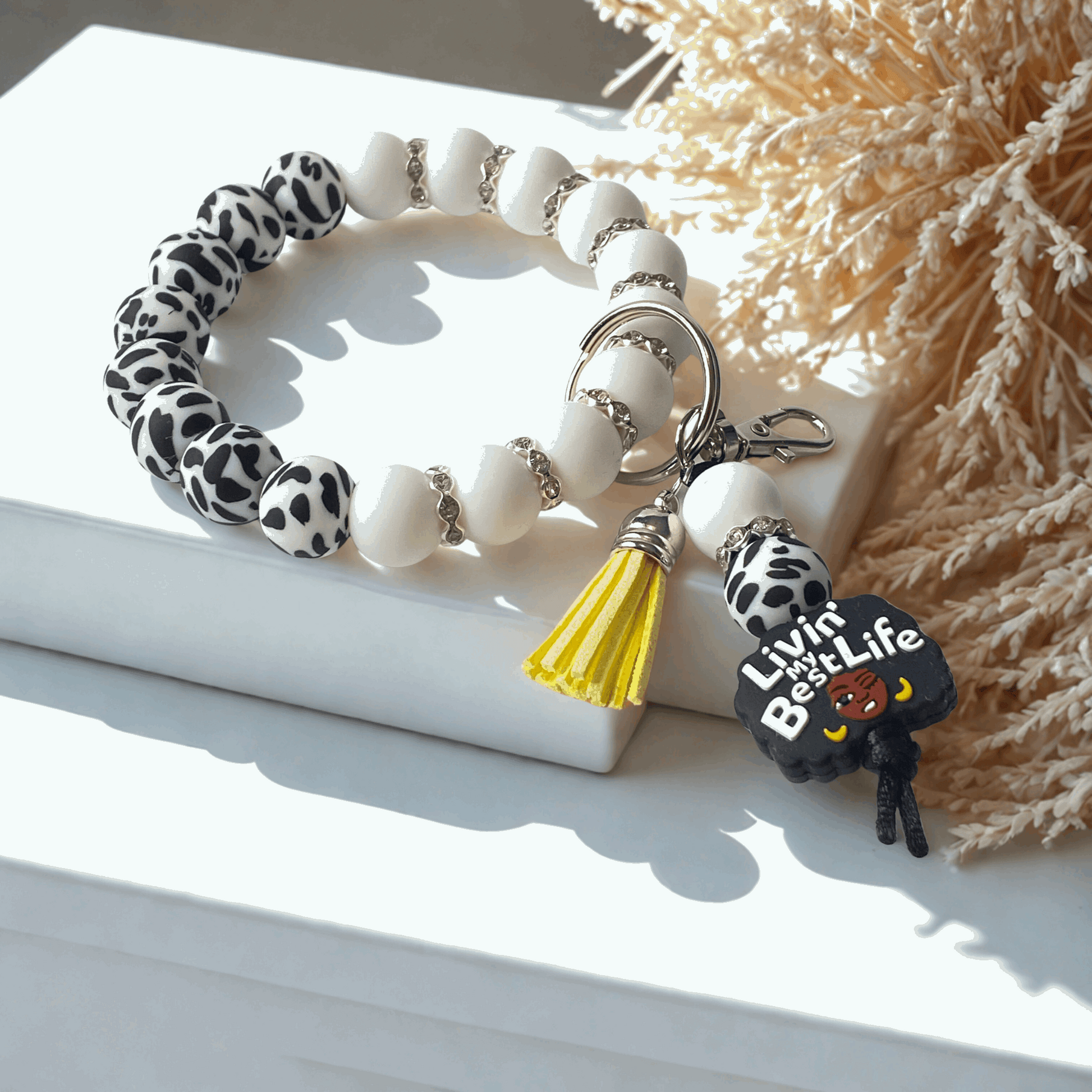 Bracelet with white beads, leopard print accents, and a keychain with a yellow tassel on a light surface.