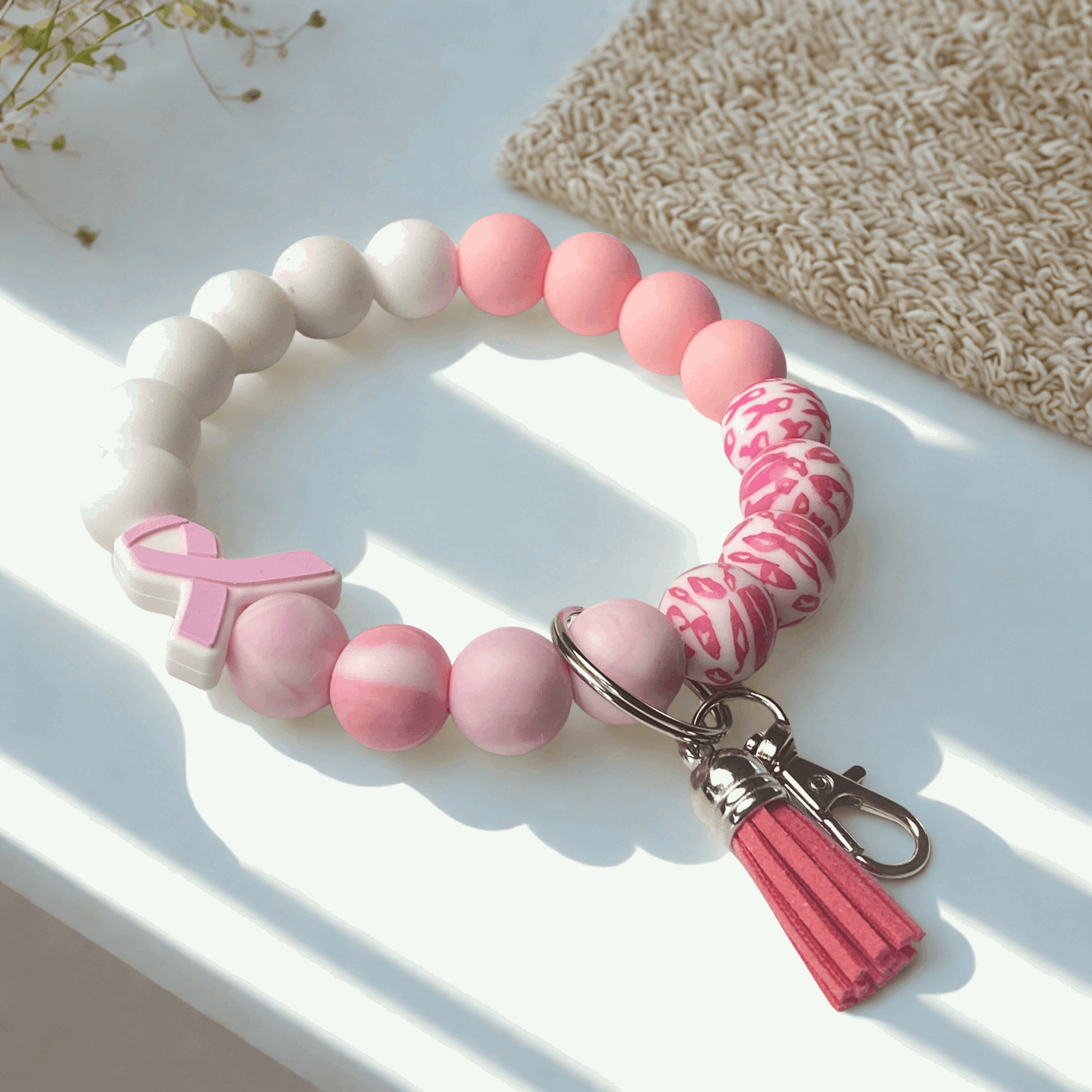 Pink and white beaded keychain with a breast cancer awareness ribbon on a light surface.
