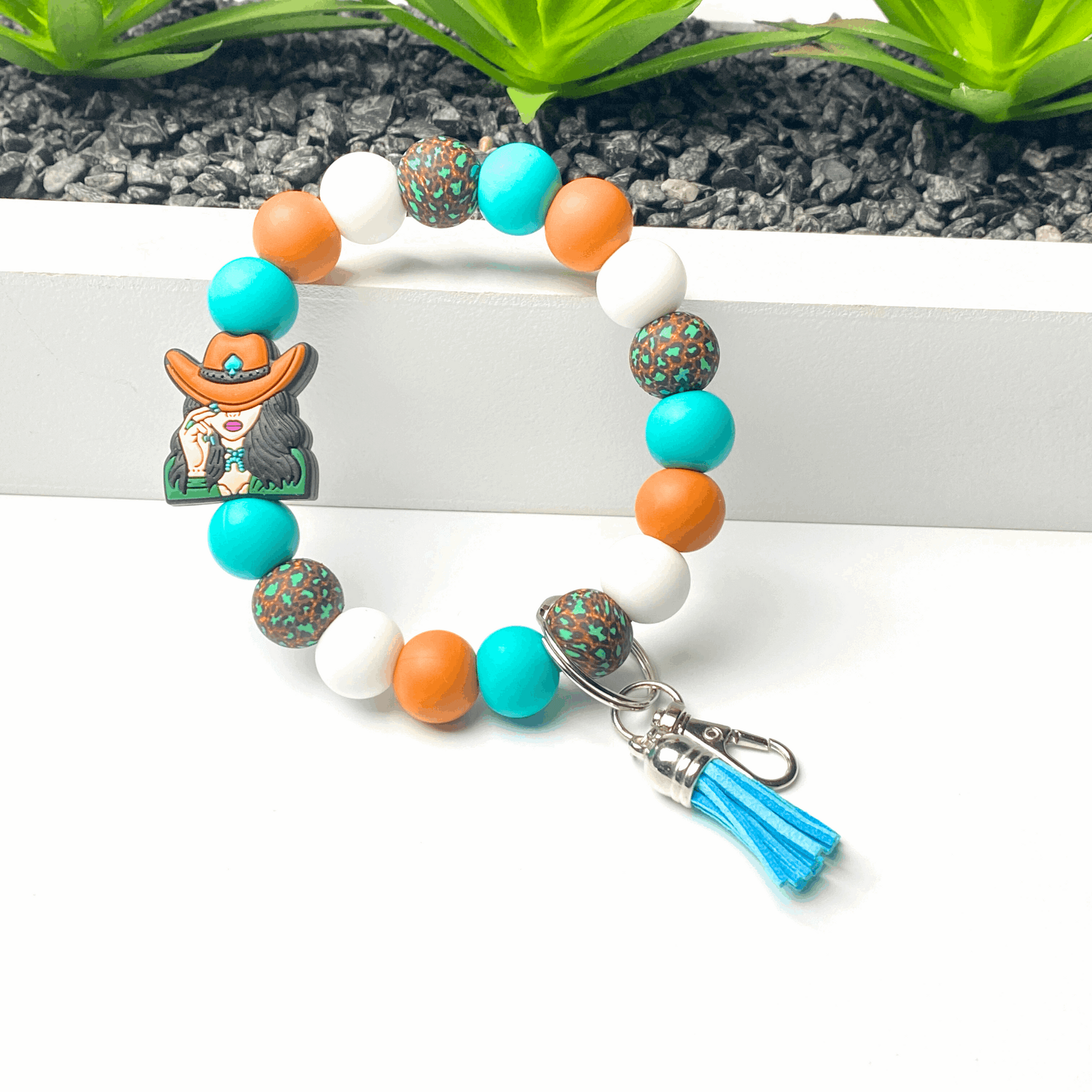 Colorful beaded bracelet with a keychain and tassel on a white surface.
