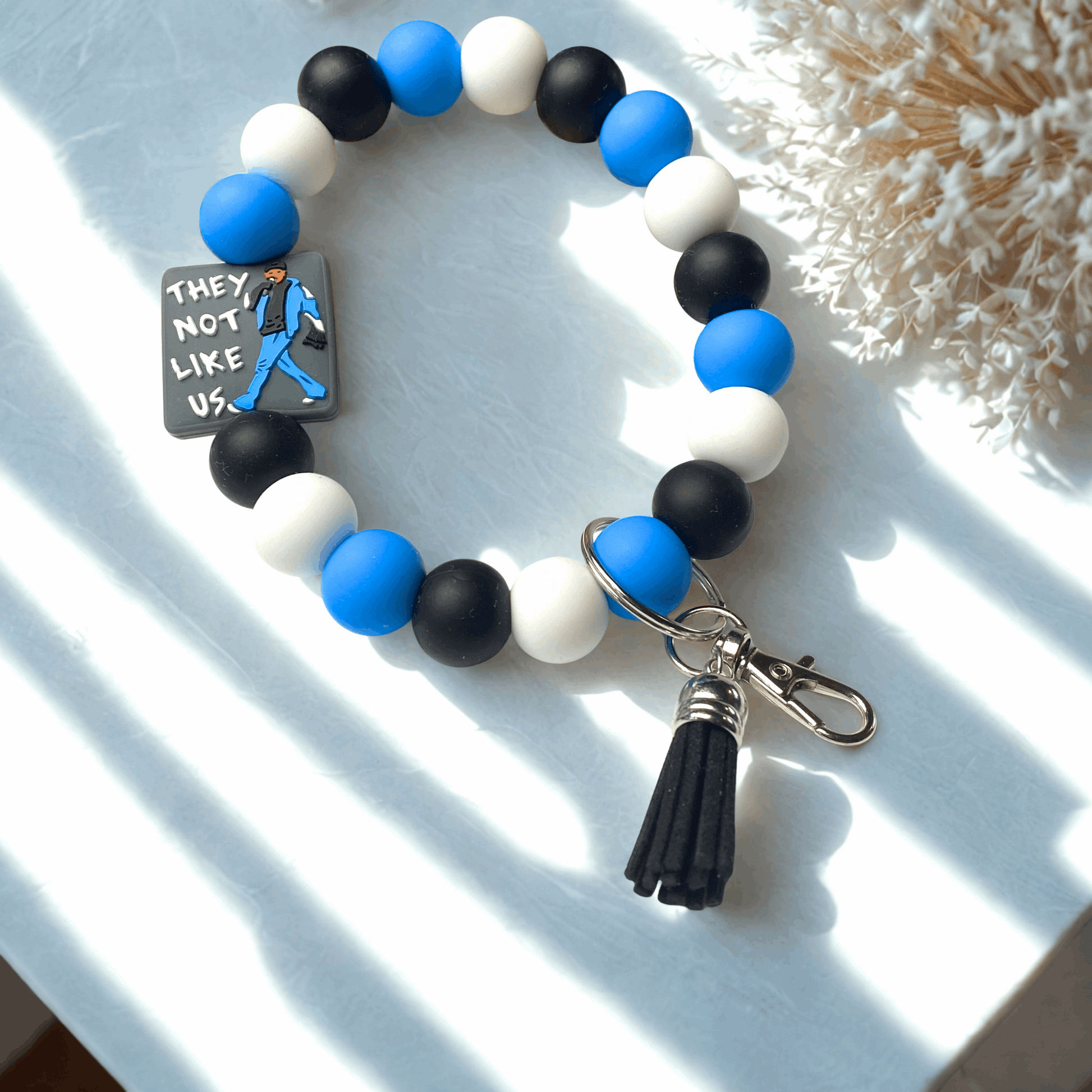 Bracelet with blue, black, and white beads and a tassel charm on a light background