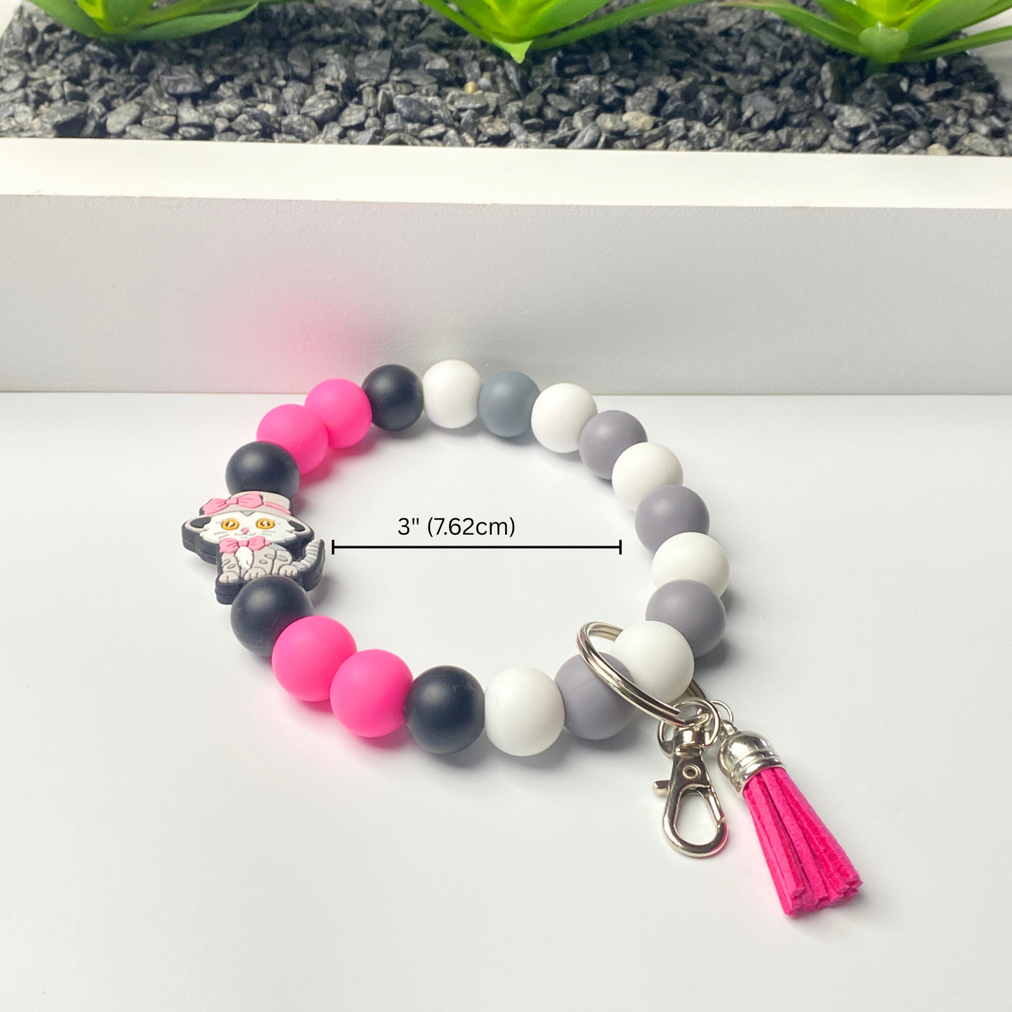 Beaded bracelet with pink, black, and white beads and a pink tassel on a white background.