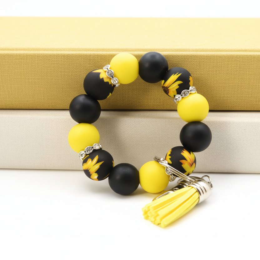 Black and yellow beaded bracelet with a tassel charm on a white surface with green plants in the background.