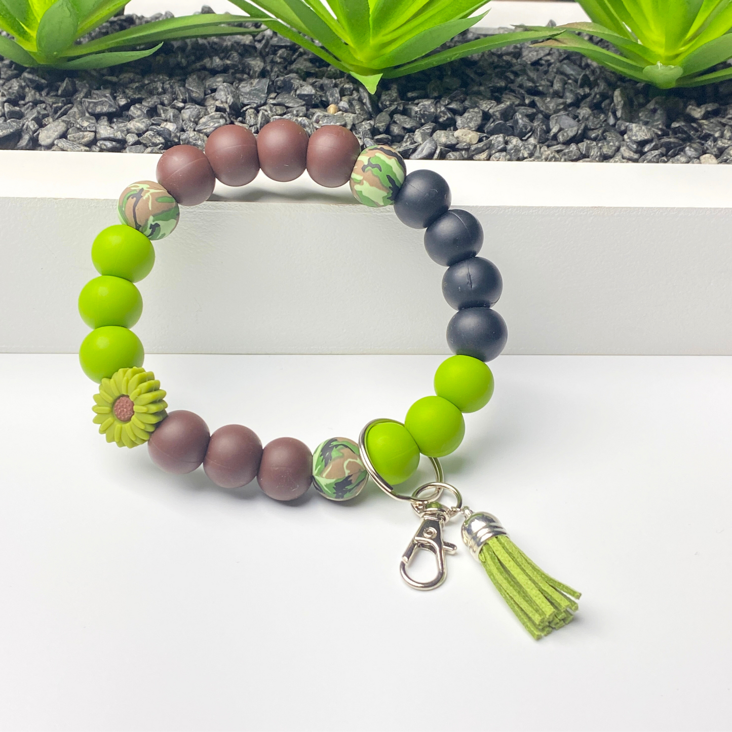 Beaded bracelet with green and brown beads and a tassel on a white background